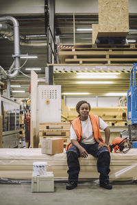 Portrait of female blue-collar worker sitting by hardhat in warehouse