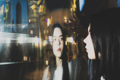 Young woman looking at reflection on window