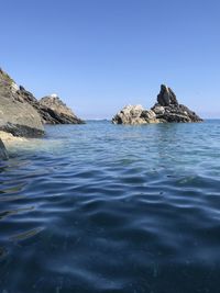 Scenic view of rocks in sea against clear blue sky