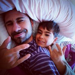 Portrait of man with his son gesturing horn sign while lying on bed