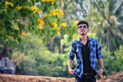 Young man wearing sunglasses standing against plants