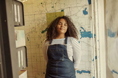 Portrait of smiling young woman standing against map