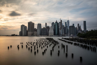 Modern buildings by river against sky during sunset