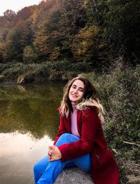 Portrait of smiling young woman sitting by lake