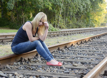 Full length of woman smoking while sitting on railroad track