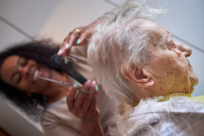 Caring african american woman caregiver, cutting her elderly woman hair at home