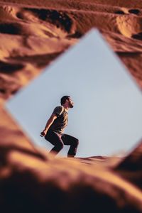 Reflection of man posing on sand in mirror