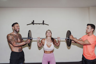 Male athletes helping female friend in exercising with barbell at gym