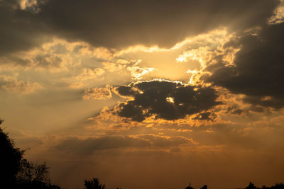 Low angle view of silhouette trees against dramatic sky during sunset