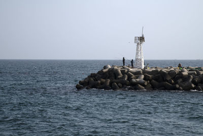 Lighthouse on rock by sea against clear sky