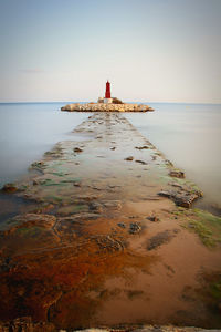 Lighthouse on beach by sea against sky