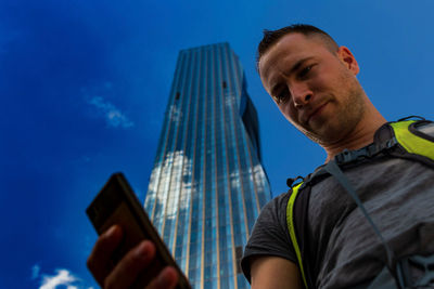 Low angle view of man using smart phone against blue sky