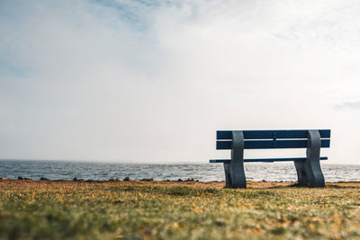 Bench on beach by sea against sky