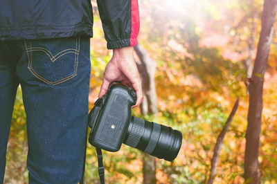 Midsection of man holding camera while standing in forest