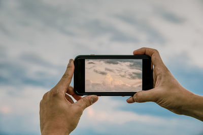 Low angle view of hand using mobile phone against sky