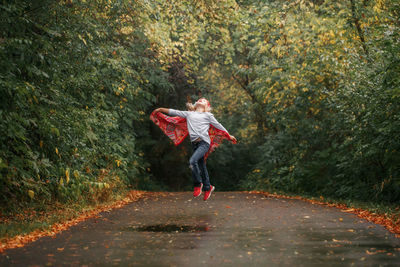 Girl jumping on road against trees in forest