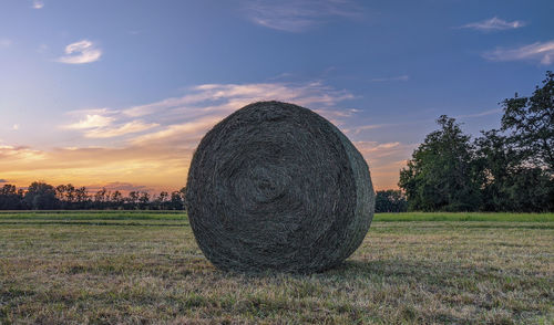 Hay bales on field against sky during sunset