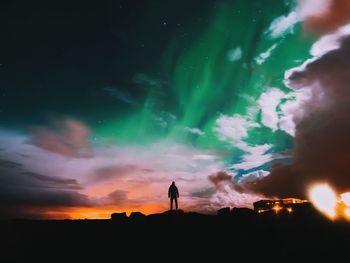 Silhouette man standing on rock by aurora borealis against cloudy sky at night