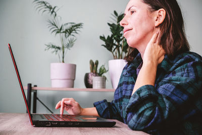 A woman suffering form neck stiffness while sitting at her laptop and working from home