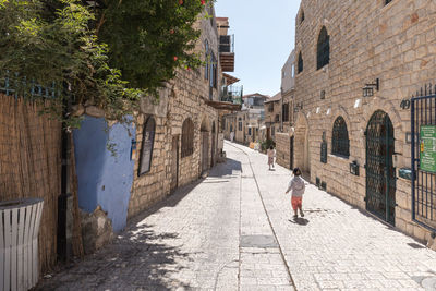 Rear view of woman walking on footpath amidst buildings in city