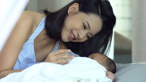 Smiling mother feeding milk to son lying on bed
