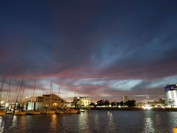 Illuminated buildings by sea against sky at sunset