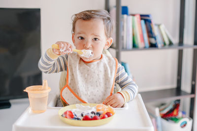 Cute caucasian baby boy eating ripe berries and fruits with yogurt. funny smiling child kid 