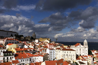 Residential buildings in city by sea against cloudy sky