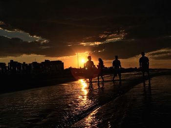 Silhouette people on beach against sky during sunset