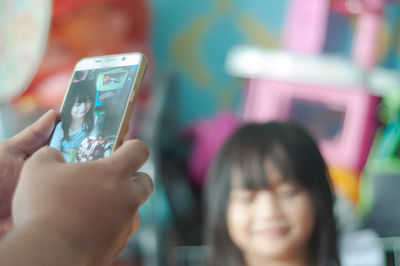 Close-up of man's hand photographing daughter with mobile phone