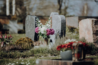 Grave stone with flowers at graveyard on sunny day with bouquet arranged on ground 