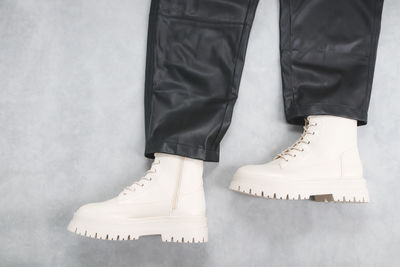 White eco-leather ankle boots with buckles, laces and black stylish leather trousers on a cement