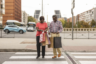 Happy couple with shopping bags crossing road in city