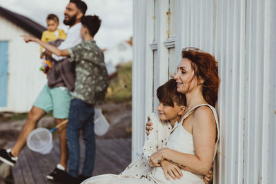 Smiling mother embracing son while family standing in background