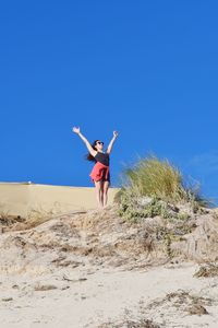 Woman with arms raised on beach against clear sky