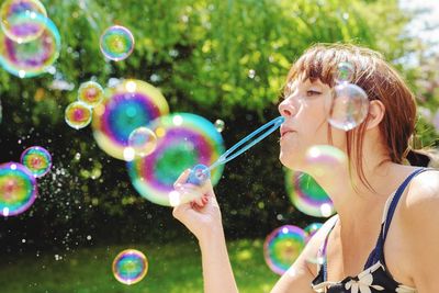 Woman blowing bubbles while standing against plants at park