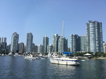 Sailboats in city by sea against clear sky