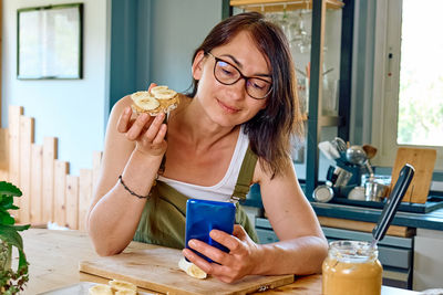 Woman enjoying her healthy breakfast checking on her smart phone at home. 