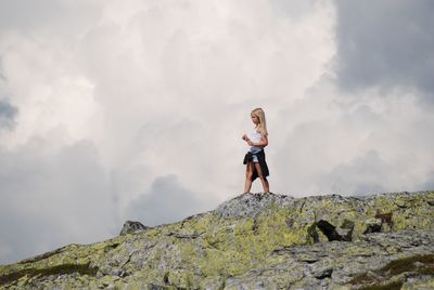 Low angle view of woman standing on rock against sky