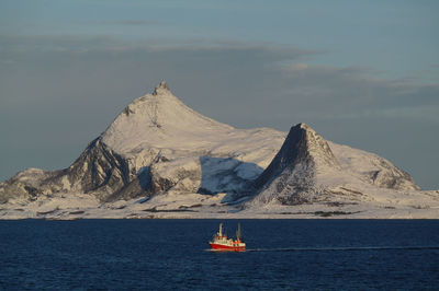 Sailboat on sea by snowcapped mountain against sky