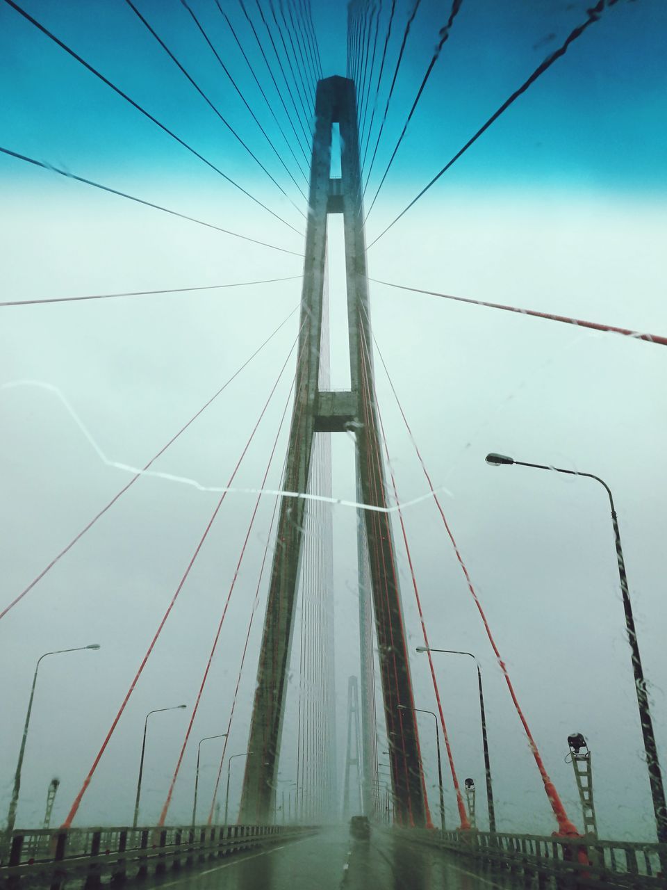 transportation, connection, the way forward, road, bridge - man made structure, cable, diminishing perspective, suspension bridge, blue, sky, engineering, day, vanishing point, surface level, in a row, long, cloud, outdoors, cable-stayed bridge, steel cable, tranquil scene, bridge