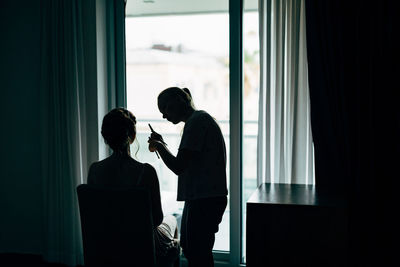 Silhouette man and woman standing by window