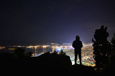 Rear view of silhouette man looking at illuminated cityscape against sky