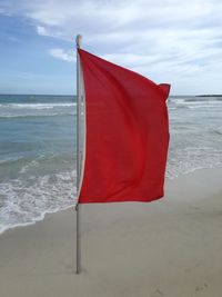 Red flag on beach against sky