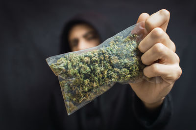 Close-up of hand holding leaf over black background