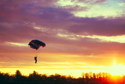 Low angle view of person paragliding over landscape flying against cloudy sky during sunset