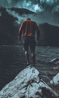 Rear view of man standing on rock against sky