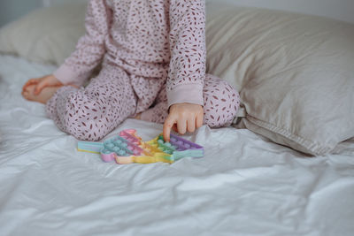 Little girl 5 years old in pink pajamas sits on the bed and plays popit. face not visible