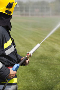 Firefighter spraying water from fire hose on field