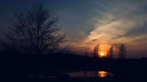 Silhouette bare tree by lake against sky during sunset